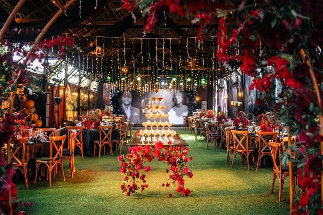 Evening reception under a canopy of red flowers, with a champagne tower and fairy lights
